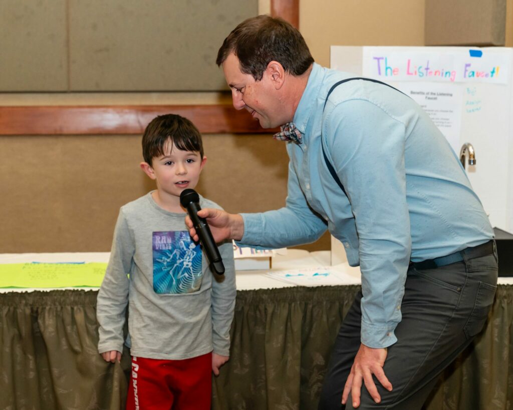 Anthony Poponi interviewing a student at a Rotary Club's “Invention Convention” which showcases elementary school finalists showing of their inventions.